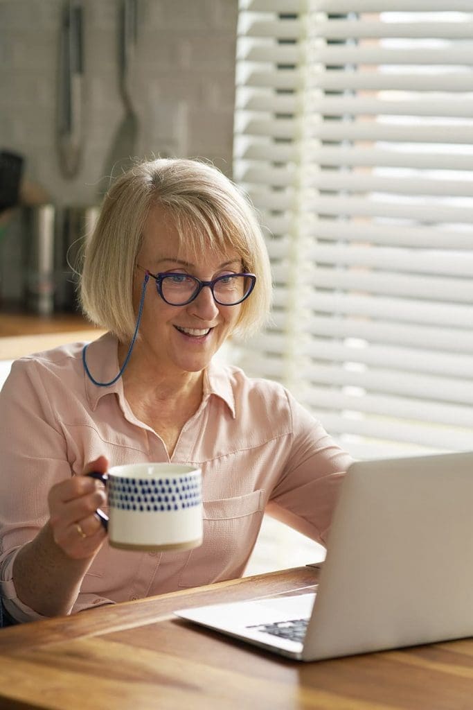 An older woman using a laptop and drinking coffee